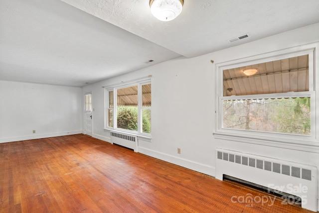 empty room featuring radiator heating unit, wood finished floors, and visible vents