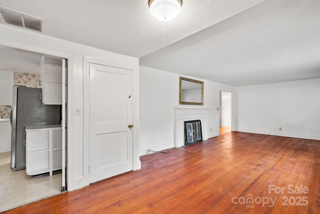 unfurnished living room featuring wood finished floors, baseboards, visible vents, a fireplace with flush hearth, and a textured ceiling