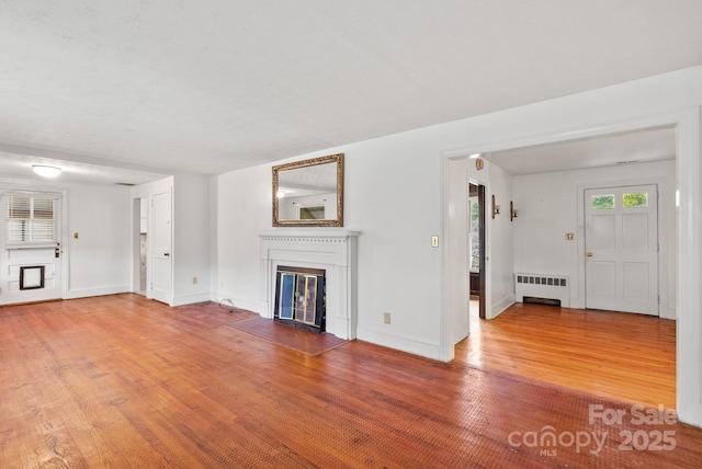 unfurnished living room featuring a glass covered fireplace, radiator heating unit, wood finished floors, and baseboards