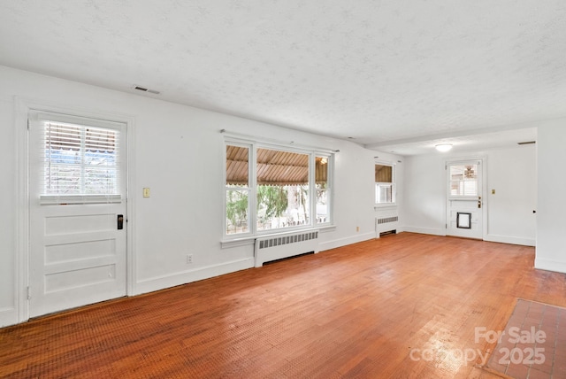 unfurnished living room with baseboards, radiator, light wood-style flooring, and a textured ceiling