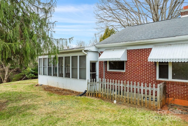 view of side of property with roof with shingles, a yard, a sunroom, a chimney, and brick siding