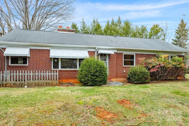 ranch-style house with a shingled roof, a front yard, brick siding, and a chimney