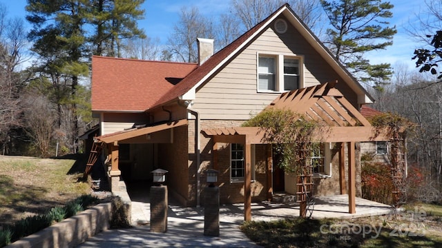 rear view of property with stone siding, a chimney, a patio, and roof with shingles