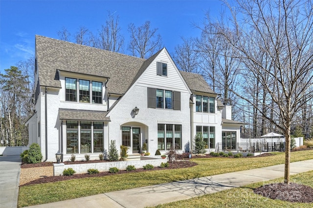 view of front of house featuring brick siding, fence, roof with shingles, a chimney, and a front yard