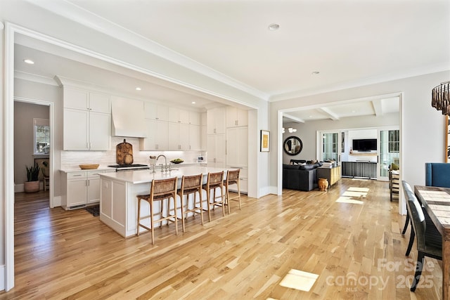 kitchen with custom exhaust hood, light wood-style flooring, open floor plan, white cabinets, and a kitchen breakfast bar