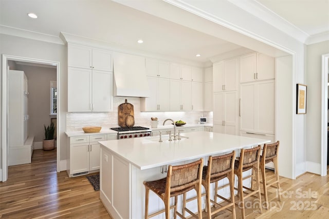 kitchen with a breakfast bar, backsplash, ornamental molding, a sink, and premium range hood