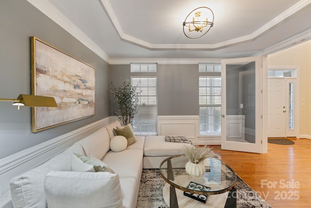 living area featuring a wainscoted wall, crown molding, a tray ceiling, and wood finished floors