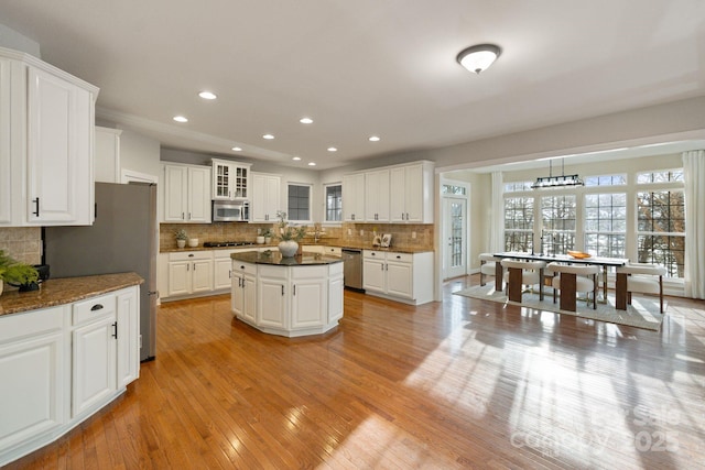 kitchen featuring a kitchen island, glass insert cabinets, stainless steel appliances, light wood-type flooring, and white cabinetry