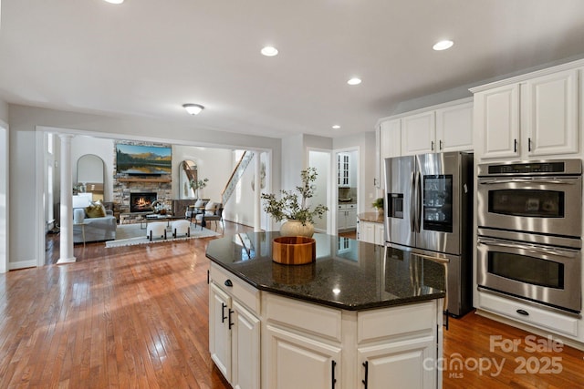 kitchen featuring recessed lighting, stainless steel appliances, a fireplace, wood-type flooring, and ornate columns