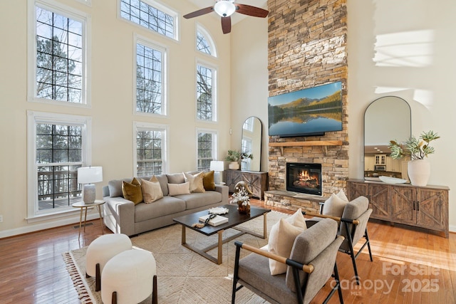 living area featuring a fireplace, a towering ceiling, ceiling fan, wood finished floors, and baseboards