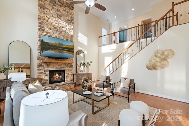 living room featuring a stone fireplace, wood finished floors, a ceiling fan, baseboards, and ornamental molding