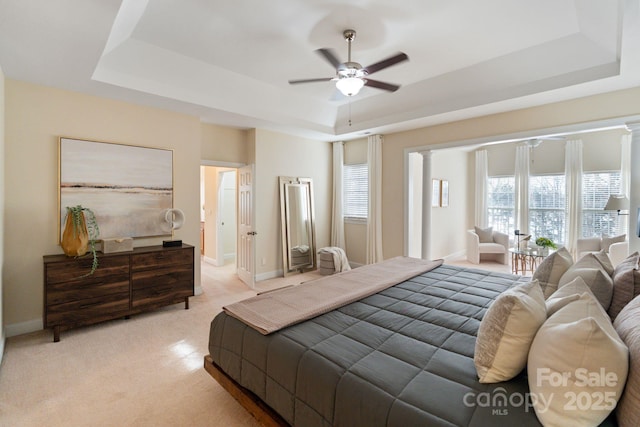 bedroom featuring light carpet, a raised ceiling, decorative columns, and baseboards