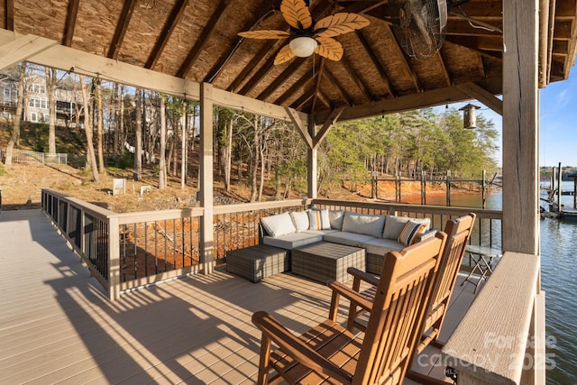 wooden terrace featuring an outdoor hangout area, a dock, a water view, and a ceiling fan