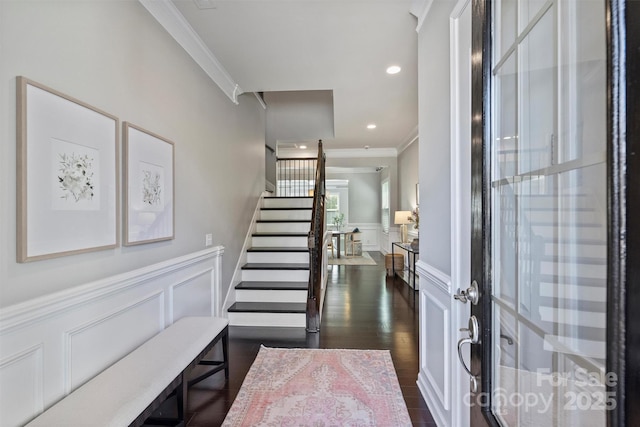 entrance foyer featuring a wainscoted wall, ornamental molding, dark wood-style floors, a decorative wall, and stairs