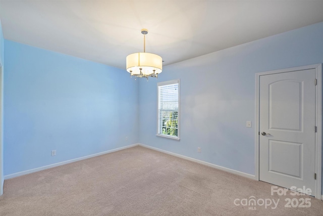 empty room featuring a notable chandelier, carpet flooring, and baseboards