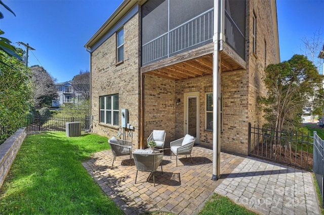 rear view of house featuring brick siding, fence, a lawn, cooling unit, and a patio