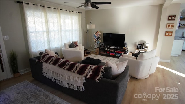 living room featuring wood finished floors, a ceiling fan, and baseboards