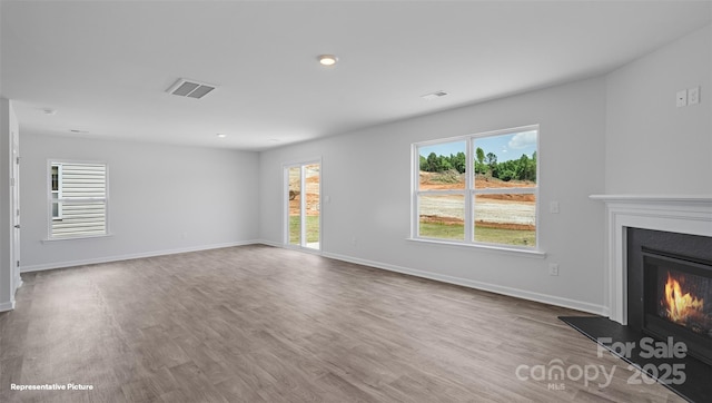 unfurnished living room featuring baseboards, visible vents, a glass covered fireplace, wood finished floors, and recessed lighting