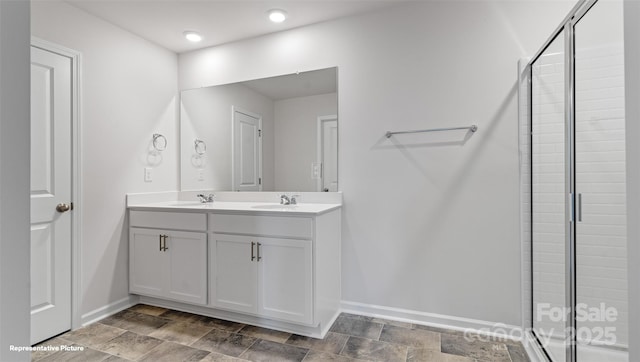 full bath featuring stone finish flooring, a sink, baseboards, a shower stall, and double vanity