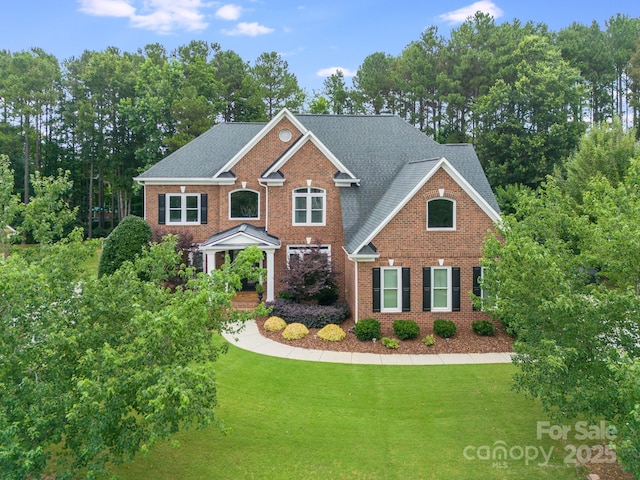 view of front of home featuring brick siding, roof with shingles, and a front yard