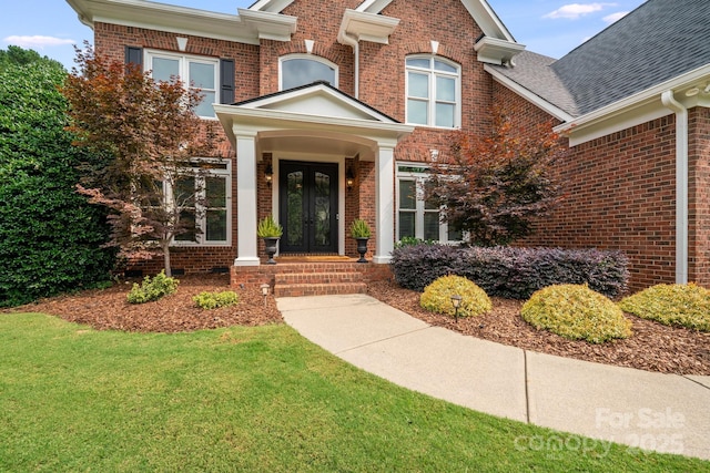 doorway to property with french doors, a lawn, a shingled roof, and brick siding