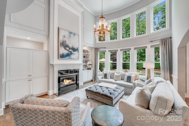 living room featuring built in features, a glass covered fireplace, a high ceiling, crown molding, and light wood-style floors