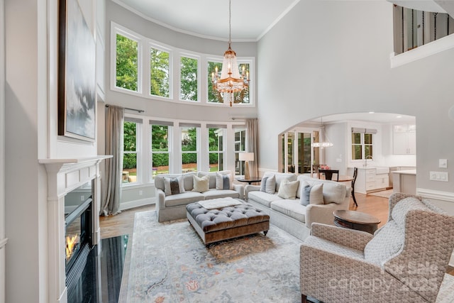 living area with a chandelier, arched walkways, wood finished floors, a glass covered fireplace, and crown molding