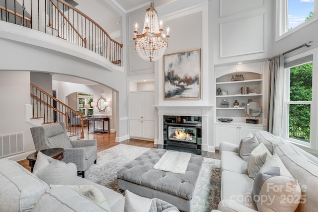 living area featuring visible vents, a fireplace with flush hearth, stairway, light wood-type flooring, and built in shelves