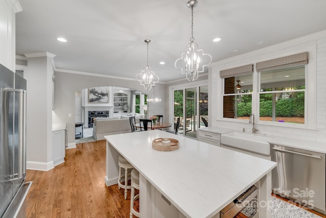 kitchen featuring a glass covered fireplace, light wood-style flooring, stainless steel appliances, crown molding, and a sink