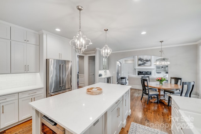 kitchen with arched walkways, crown molding, high end fridge, light countertops, and wood finished floors