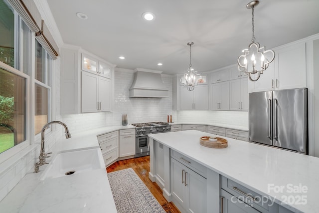 kitchen with tasteful backsplash, high end appliances, custom exhaust hood, pendant lighting, and a sink