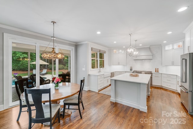 kitchen featuring a center island, ornamental molding, wood finished floors, premium range hood, and high end refrigerator