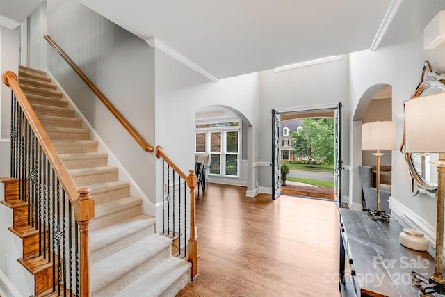 foyer featuring arched walkways, stairway, ornamental molding, wood finished floors, and baseboards