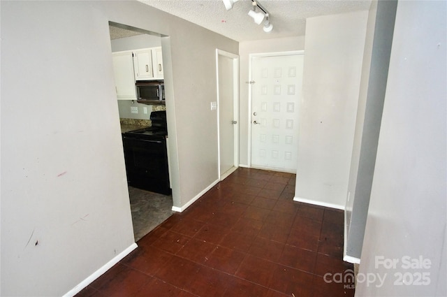 hallway featuring track lighting, a textured ceiling, and baseboards