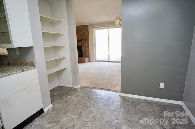 interior space featuring built in shelves, a fireplace, carpet flooring, and baseboards