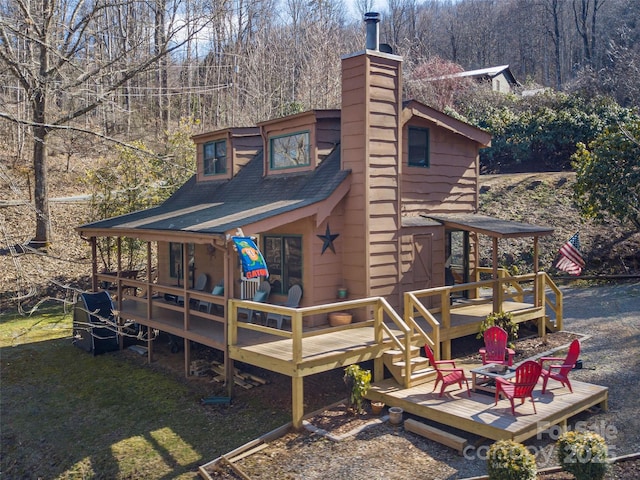 rear view of house featuring roof with shingles, a chimney, a deck, and a yard