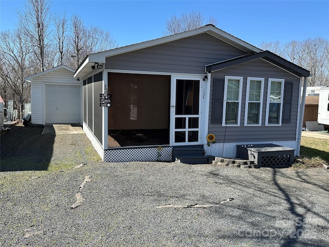 rear view of house with a detached garage, entry steps, a sunroom, driveway, and an outdoor structure