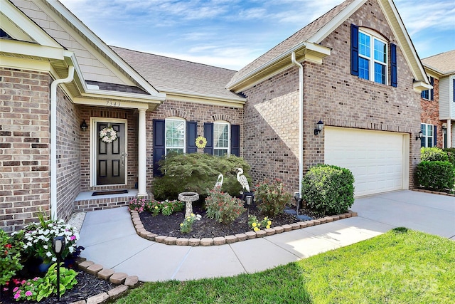 entrance to property featuring an attached garage, driveway, brick siding, and a shingled roof