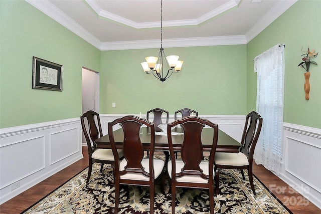 dining area with dark wood-type flooring, a tray ceiling, wainscoting, and a notable chandelier