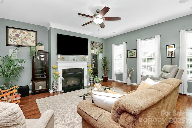 living area featuring a fireplace with flush hearth, ceiling fan, wood finished floors, and baseboards