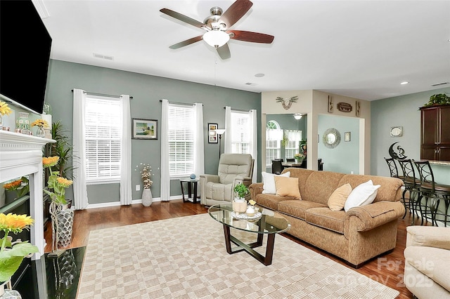 living room with wood finished floors, a ceiling fan, visible vents, baseboards, and a glass covered fireplace