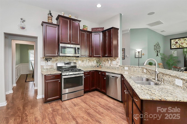 kitchen featuring light wood-style flooring, appliances with stainless steel finishes, light stone counters, a peninsula, and a sink