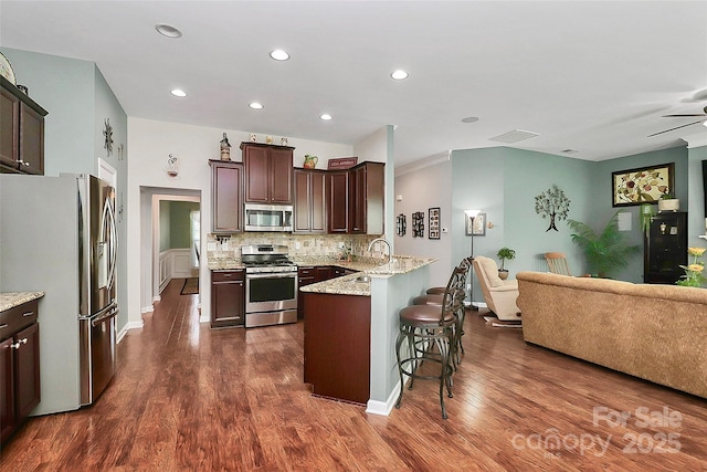 kitchen with dark brown cabinetry, stainless steel appliances, a peninsula, open floor plan, and decorative backsplash