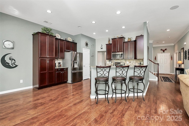 kitchen featuring visible vents, decorative backsplash, appliances with stainless steel finishes, a kitchen breakfast bar, and a peninsula