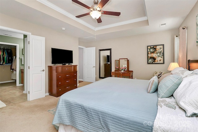 bedroom with a tray ceiling, crown molding, light colored carpet, visible vents, and a spacious closet