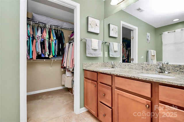 bathroom featuring visible vents, double vanity, a sink, and a walk in closet