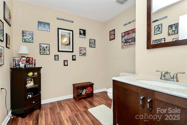 half bathroom featuring visible vents, baseboards, toilet, wood finished floors, and vanity