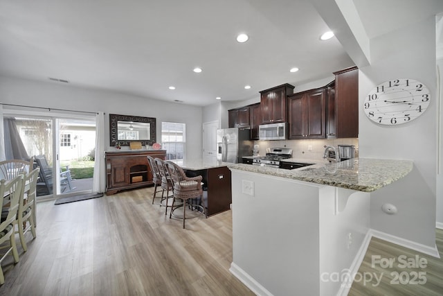 kitchen featuring appliances with stainless steel finishes, light wood-style floors, decorative backsplash, and a kitchen bar