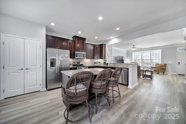 kitchen with a kitchen island, appliances with stainless steel finishes, open floor plan, a peninsula, and dark brown cabinets