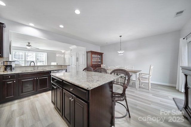 kitchen featuring a sink, light wood finished floors, backsplash, and a kitchen bar